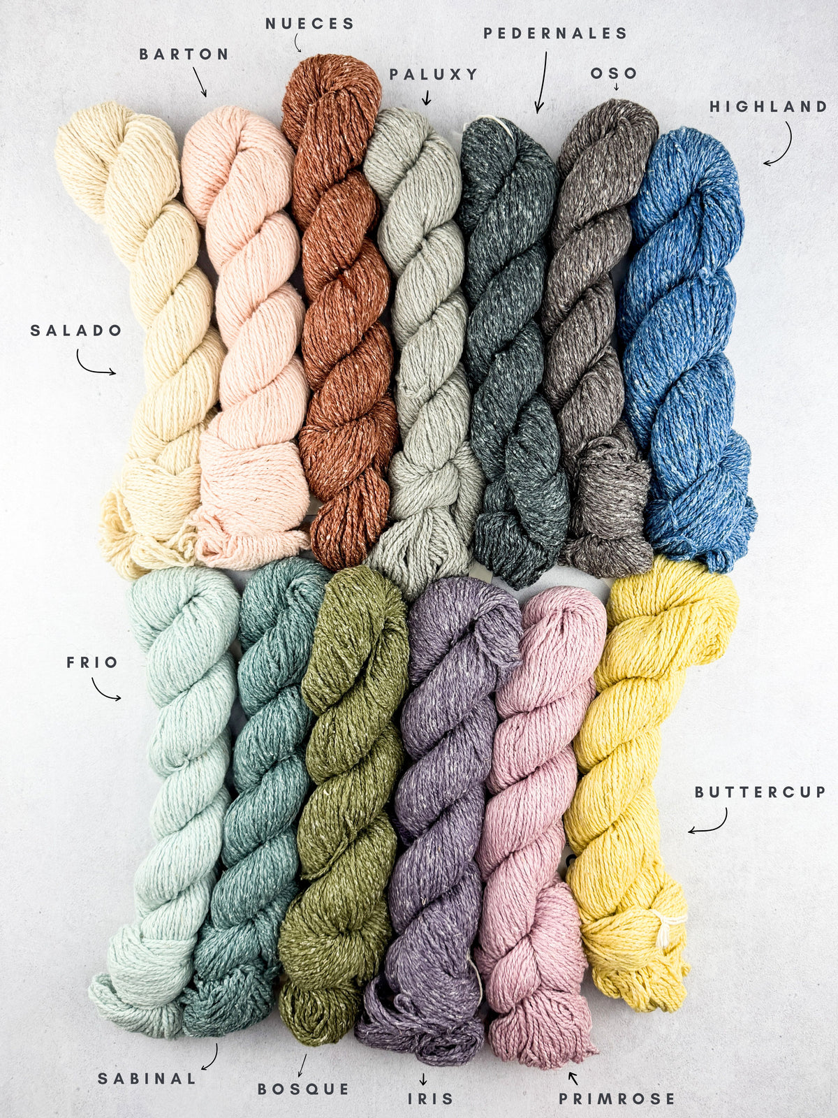 Twisted yarn skeins arranged in two rows on a light background with handwritten labels pointing to each colorway: Salado, Barton, Nueces, Paluxy, Pedernales, Oso, Highland, Frio, Sabinal, Bosque, Iris, and Primrose.